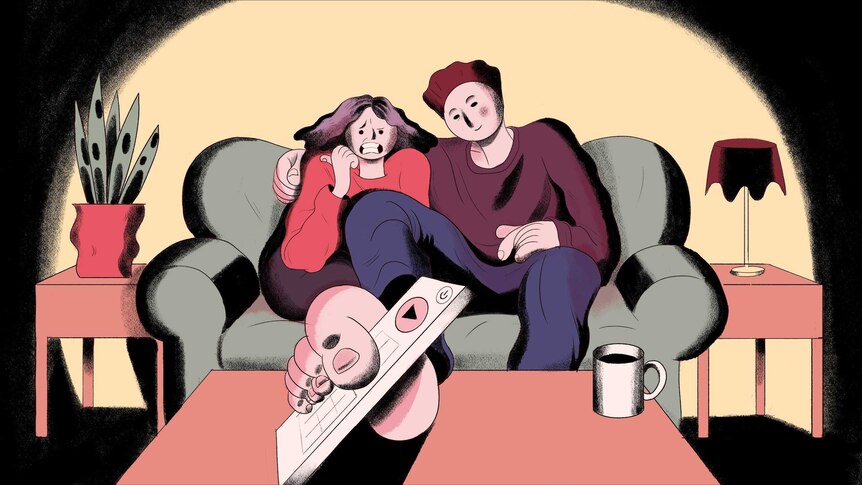 a girl and guy sitting on a couch watching tv and the guy picks up the remote with his toes
