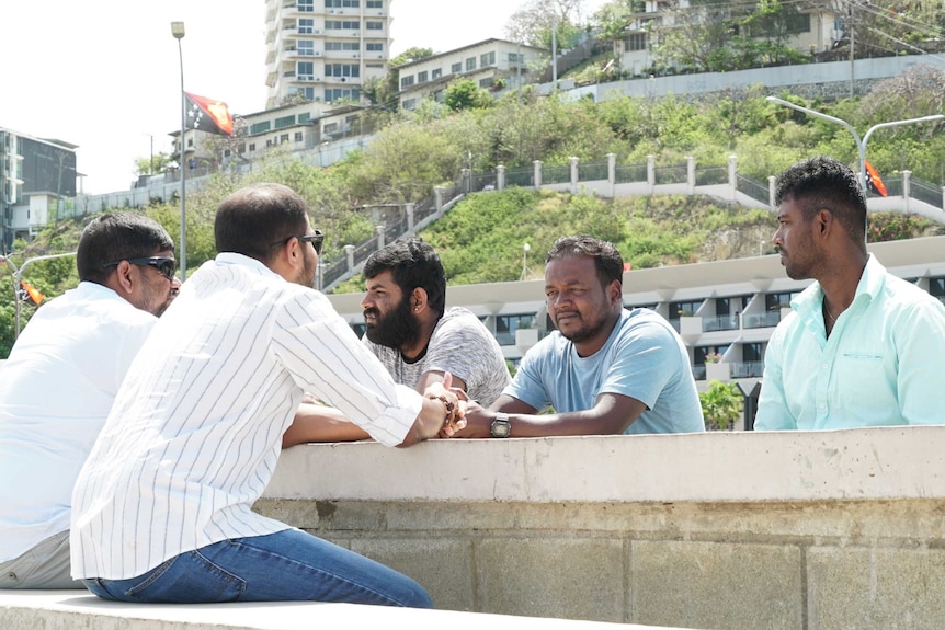 Sri Lankan refugees sit around a stone outdoors table in Port Moresby. They were previously held on Manus Island.