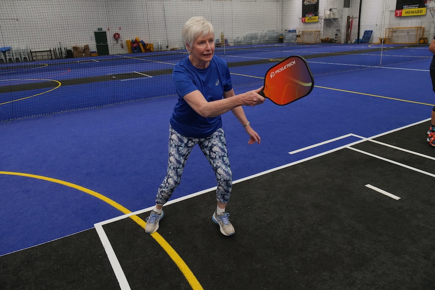 A woman holds a paddle out in front of her on an indoor court.