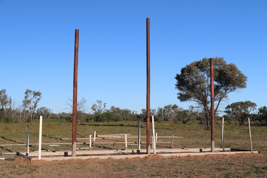 Three poles stand in the ground, early signs of construction.