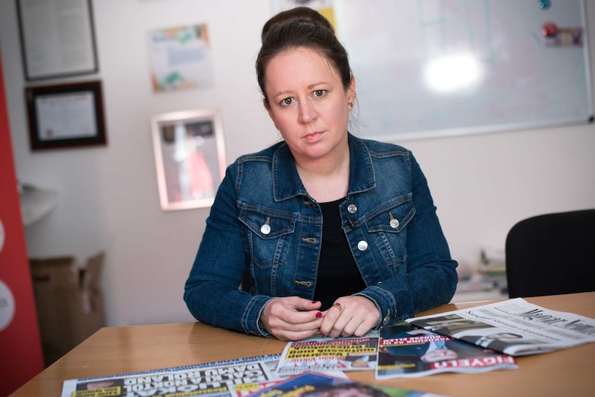 A woman looks concerned on a table with Hungarian printed media laid out in front of her.