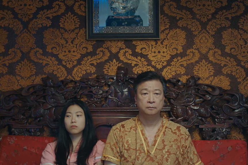 A young Chinese woman and her father sitting on a bed looking sad