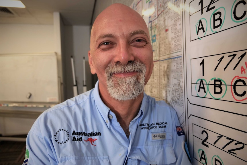 Smiling man wearing a blue Ausmat shirt leaning against a crazy wall