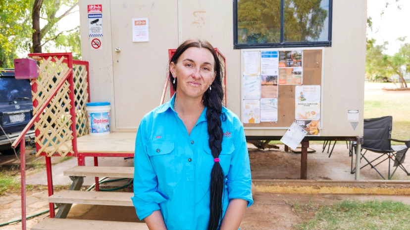 Caravan park owner stands in front of office smiling at camera. 