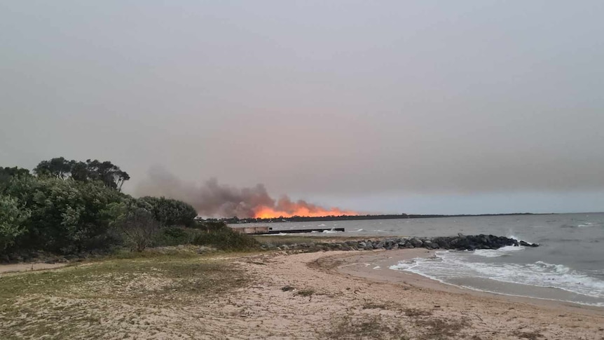 A bushfire is seen in the background behind a sandbar on a quiet beach