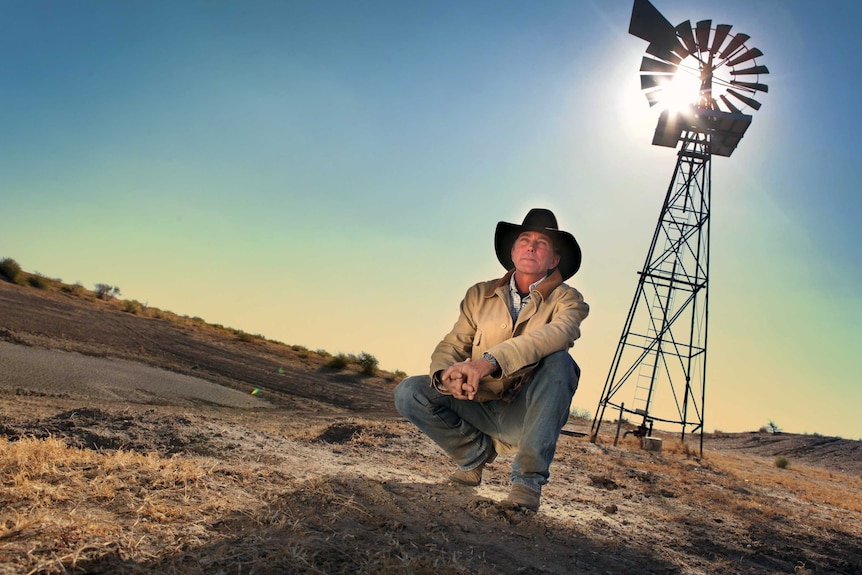 Brad Brazier crouches in front of a windmill outside Moree.