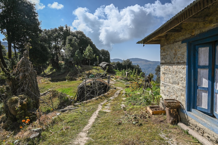 Farm life is visible next to a stone house with blue windows and mountains in the distance