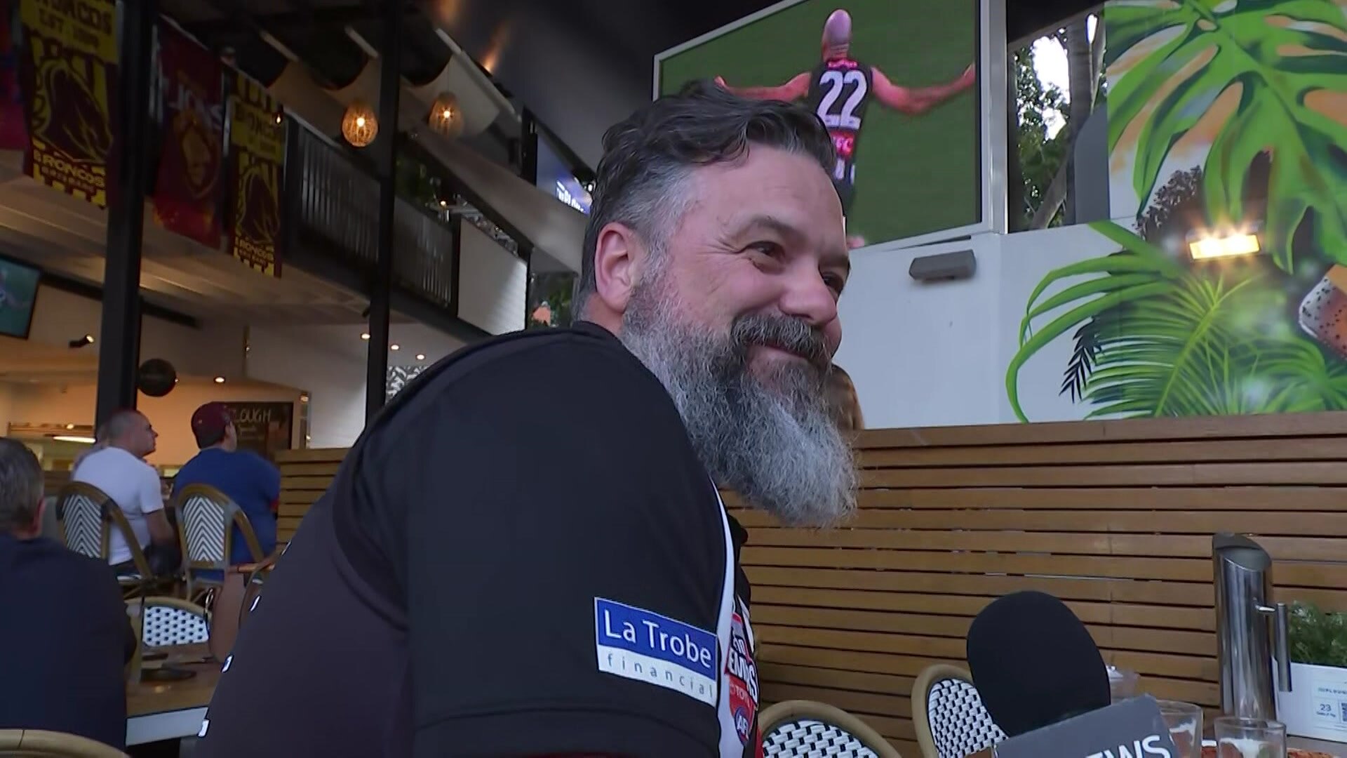 A man at a pub watching a Collingwood footy game.