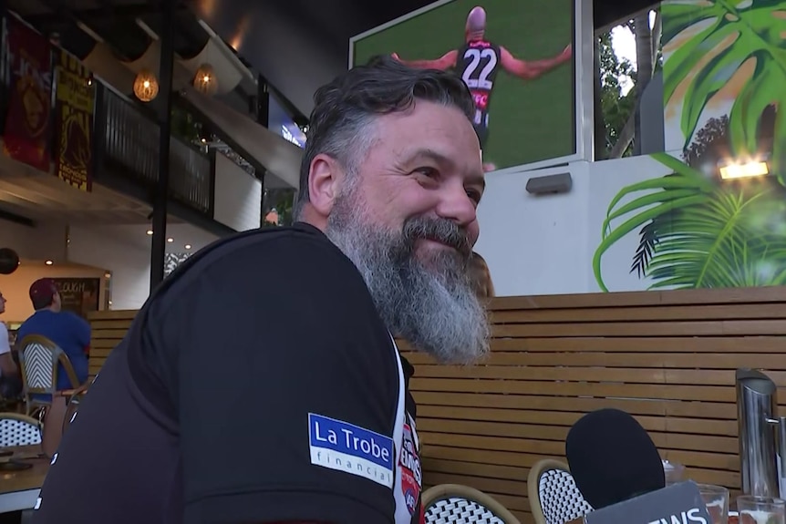 A man at a pub watching a Collingwood footy game.