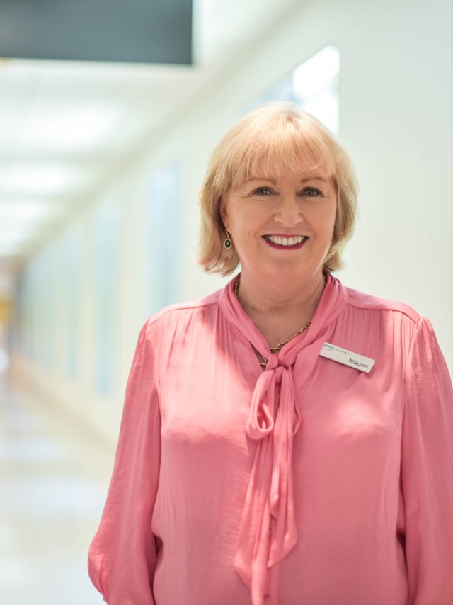Une femme blonde vêtue d'un haut clair se tenant dans un couloir d'hôpital.