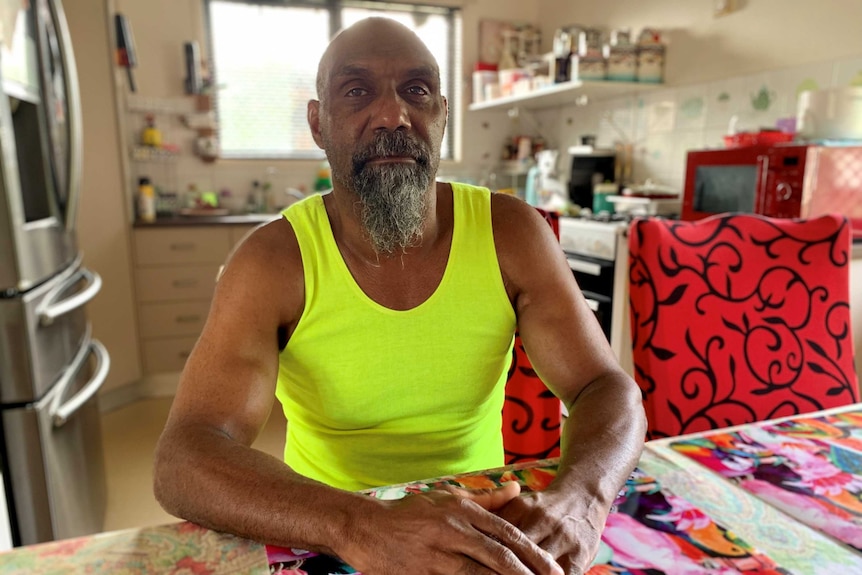 Lex Wotton, a man wearing a yellow singlet sits at a table in a kitchen