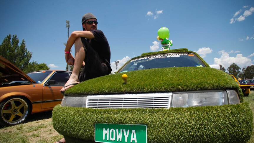 A man sits on his car, which is completely covered with artificial grass, at the Summernats festival in Canberra.