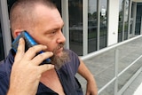 Phillip Taylor stands talking on his mobile phone outside a building.
