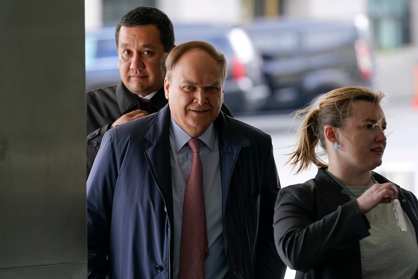 A woman and two men walk into an official building while showing their security credentials.