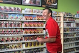 Man in red shirt standing in front of shelves of DVDs laughing.