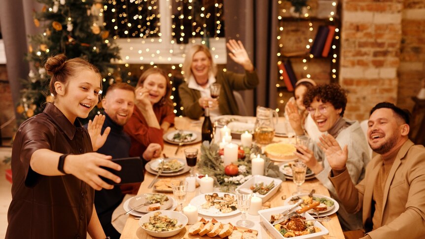Family gathered around a Christmas table laughing and waving.