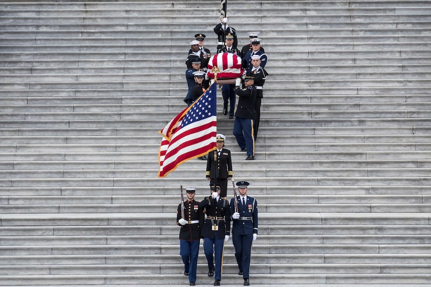 Military pallbearers carry President George HW Bush down steps.