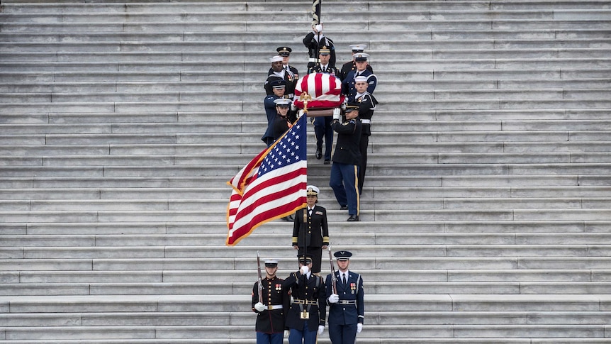 Military pallbearers carry President George HW Bush down steps.