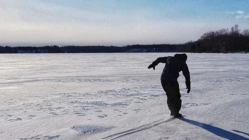 Alex McClintock dressed in black snow gear sliding on a frozen river in Canada.