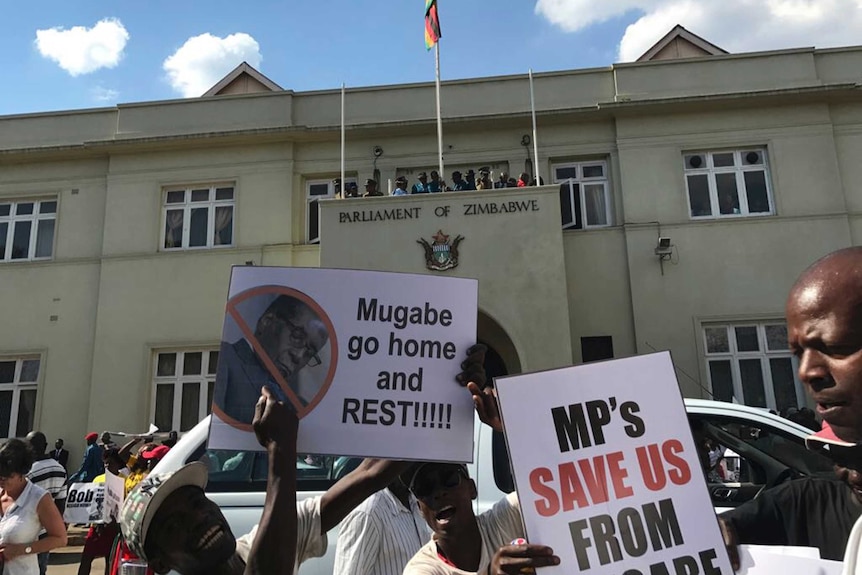 Demonstrators hold up signs outside Zimbabwean Parliament.