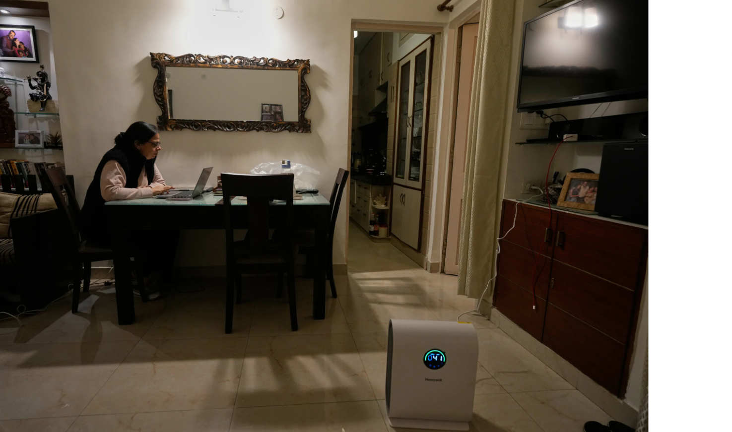 Una mujer india sentada en una mesa y utiliza un purificador de aire en el suelo.