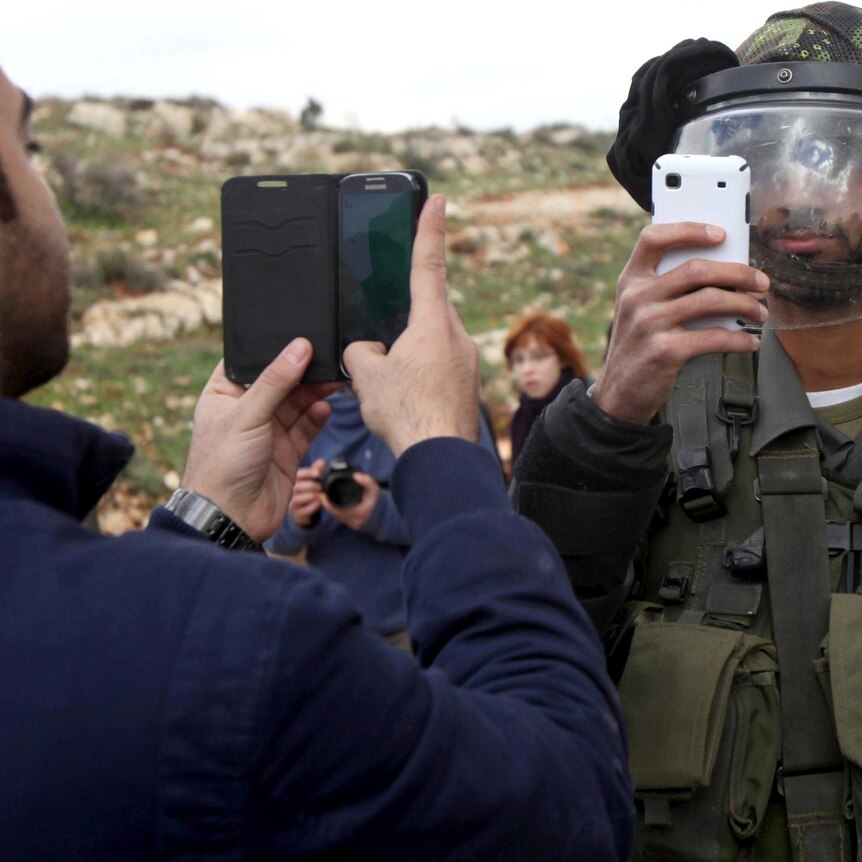 A Palestinian man and a member of the Israeli security forces take photos of each other.