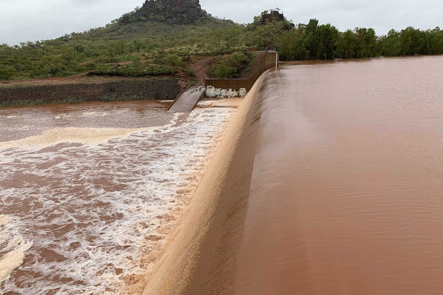 Brown water spills over the dam wall at Chinaman Creek Dam.