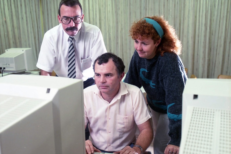 Three office workers look at a computer in the 1990s.