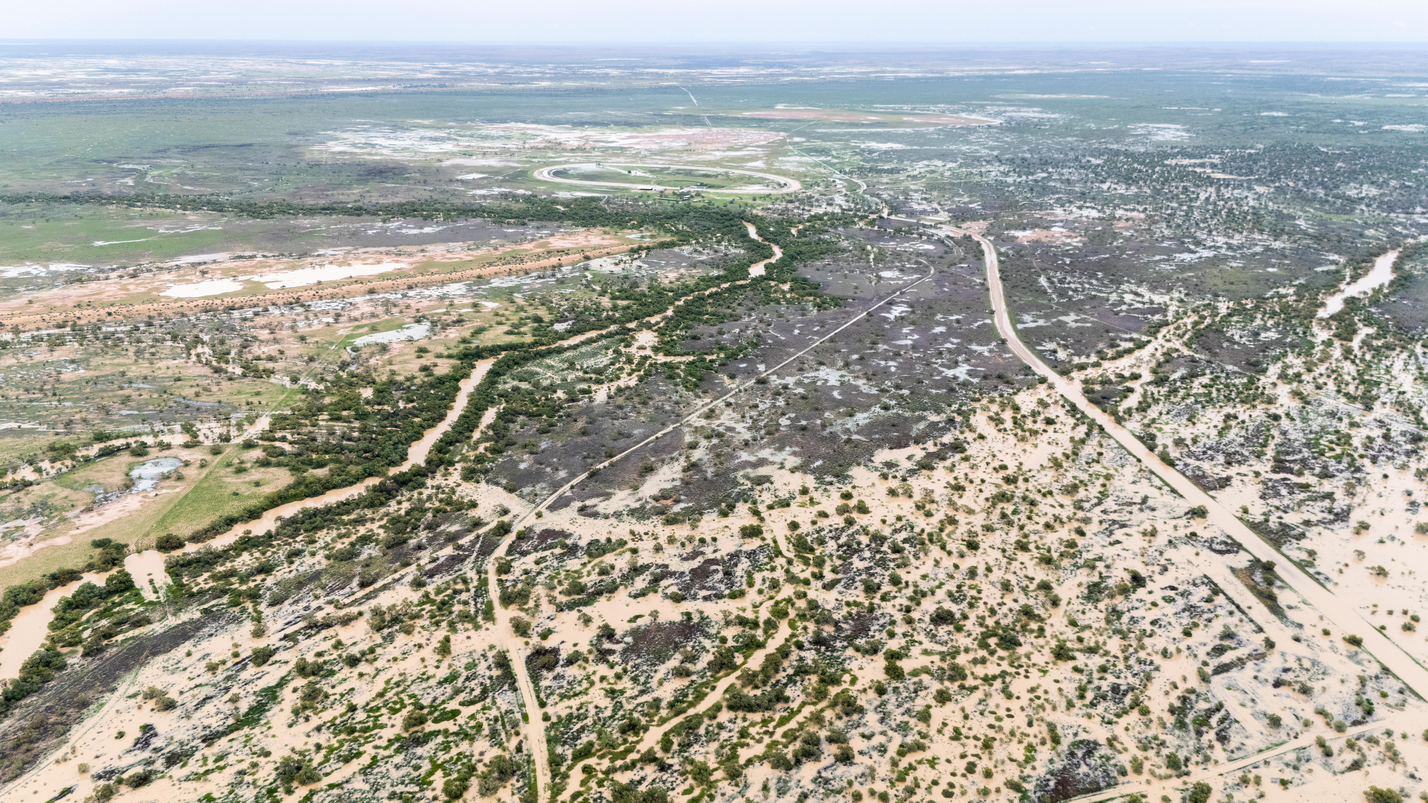 Murky brown floodwater spills out of a swollen river across floodplains in outback Queensland.