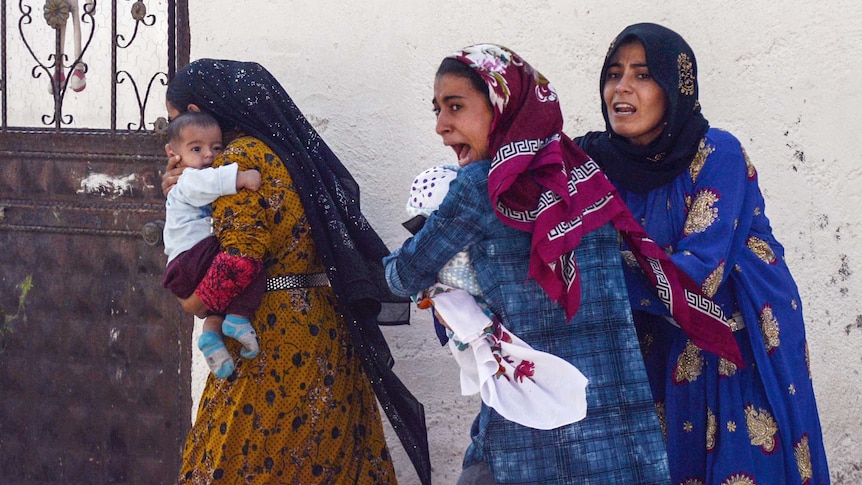 Women holding babies scream as they run near a building.