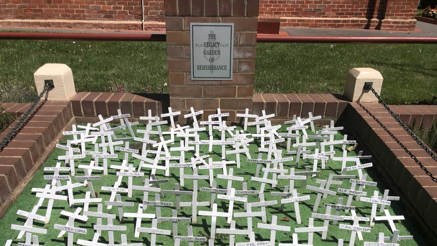 War crosses, some of the bent and damaged, sit wedged in grass with the words 'The Legacy Garden of Remembrance' written behind.