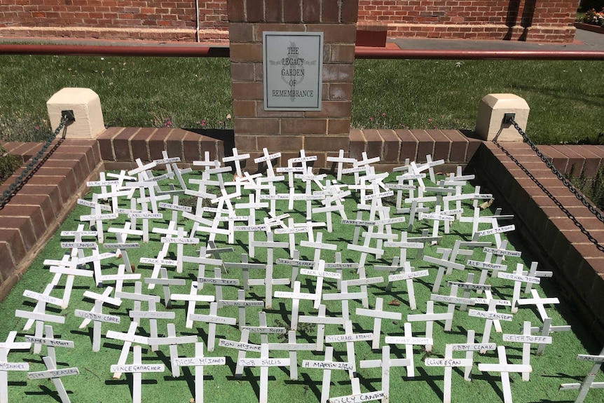 War crosses, some of the bent and damaged, sit wedged in grass with the words 'The Legacy Garden of Remembrance' written behind.