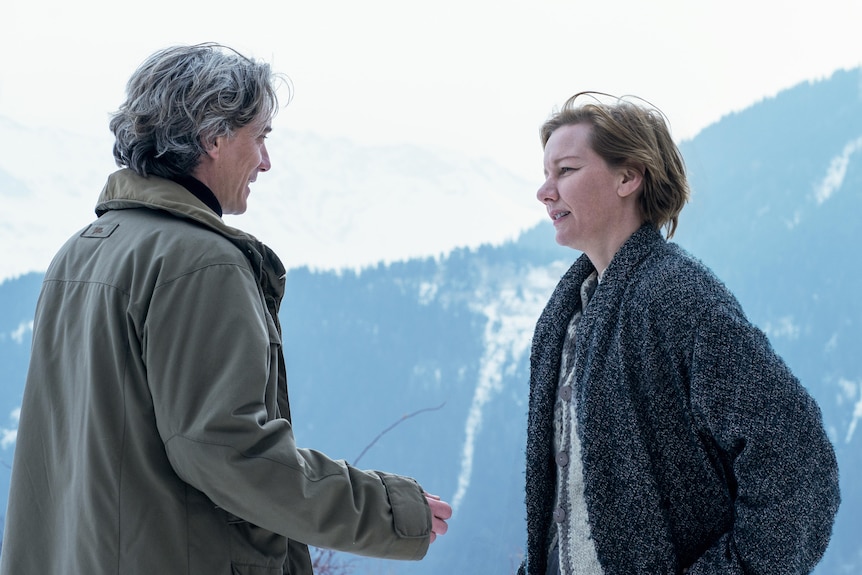 A film still of Swann Arlaud Sandra Hüller talking together in the snow. They are both wearing heavy coats.