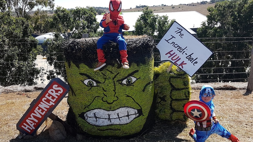 Hay bale stacked and painted to look like Incredible Hulk with children posing on top and next to it