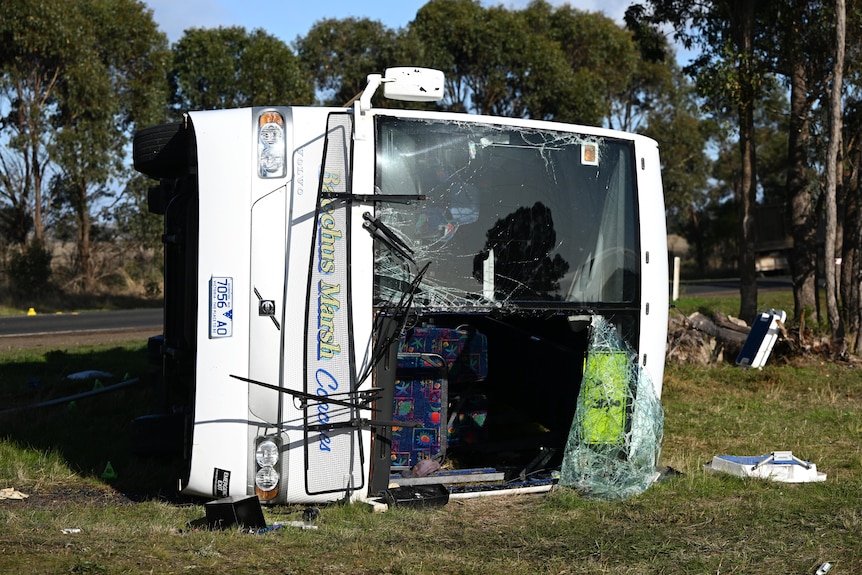 A badly damaged bus on its side near a road.