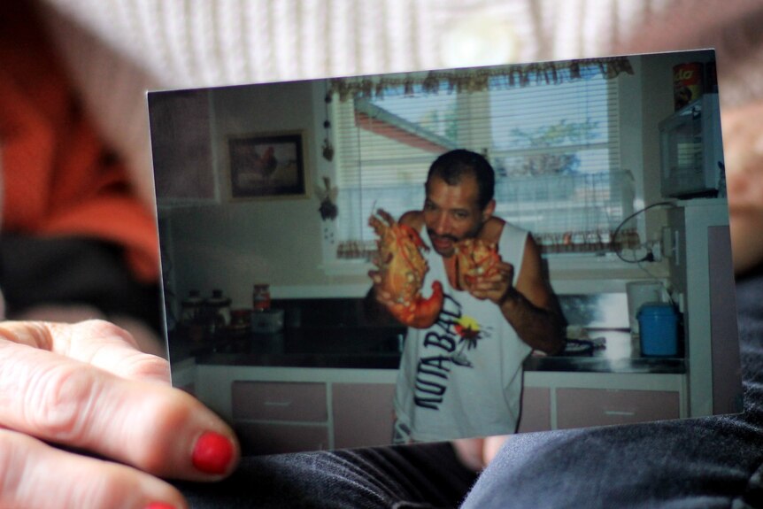 A photo of a photo of a man with olive skin holding two lobsters. The hand holding the photo has red nails.