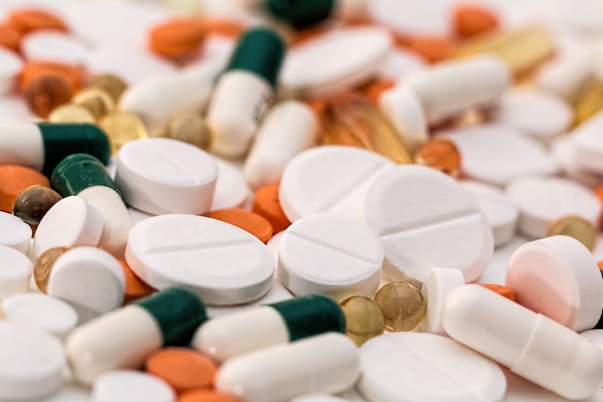 Bunch of white, oval medication tablets and white medication capsules.