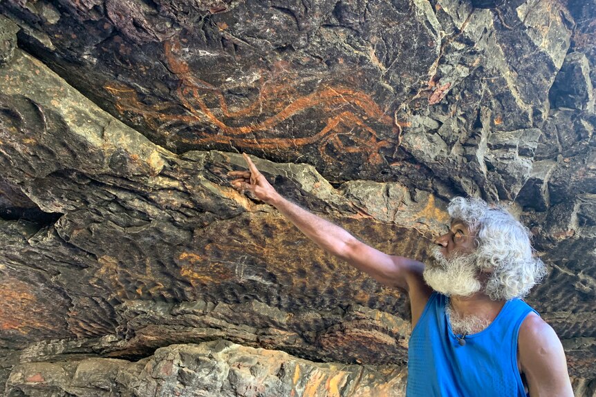 Jeffrey Lee points to rock art on a rock wall in Kakadu.