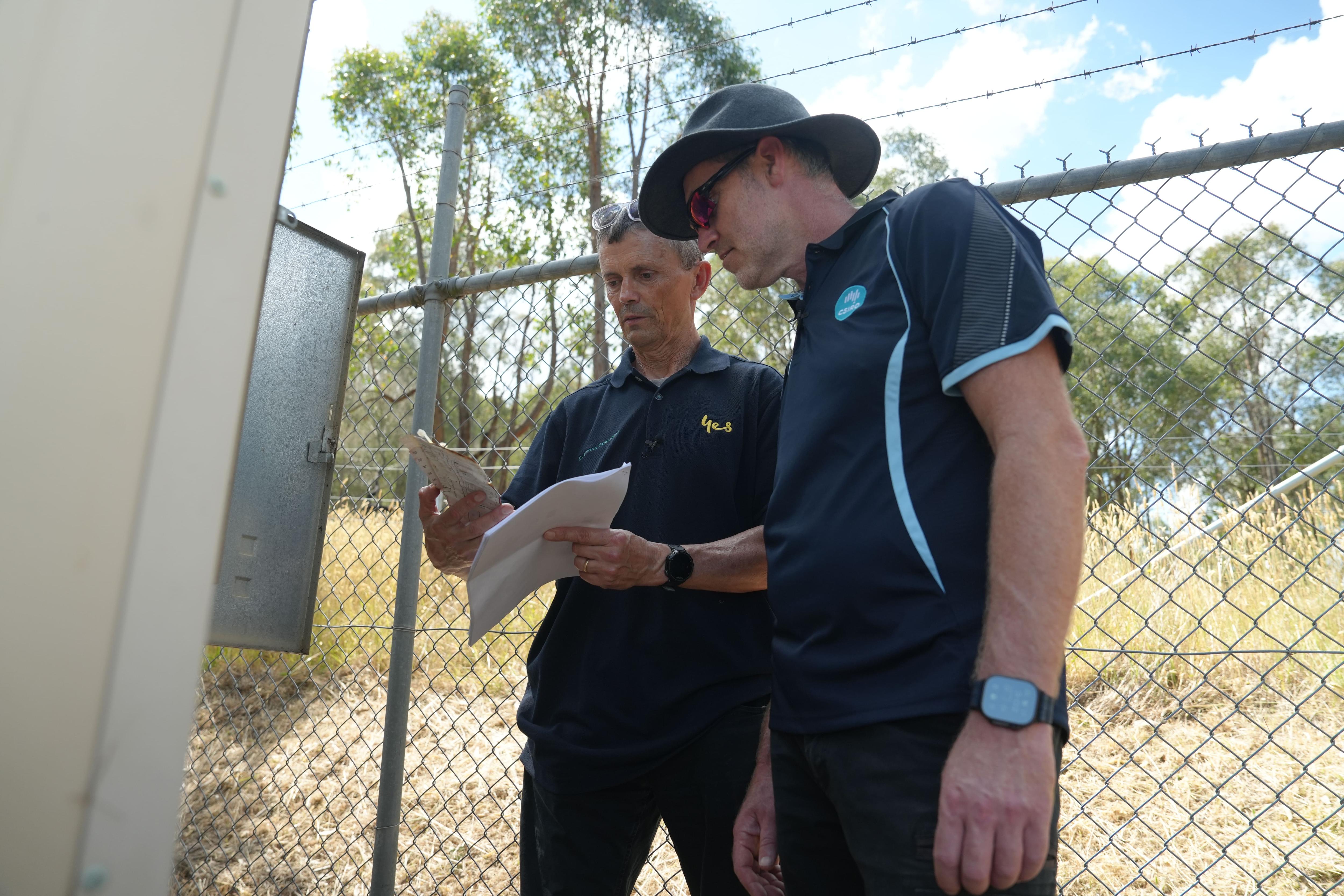 Jayson Rule and Justin Leonard both look at documents near a phone tower.