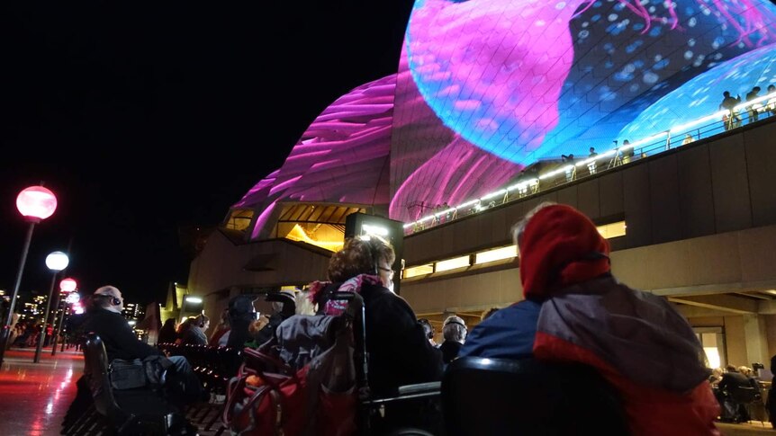Vision impaired people listen to the description of a light display on the western sails of the Opera House.
