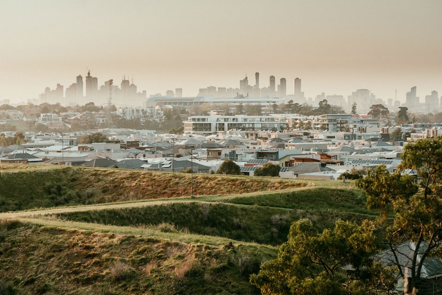 Large grassy mounds surrounded by houses with a CBD skyline in the background.