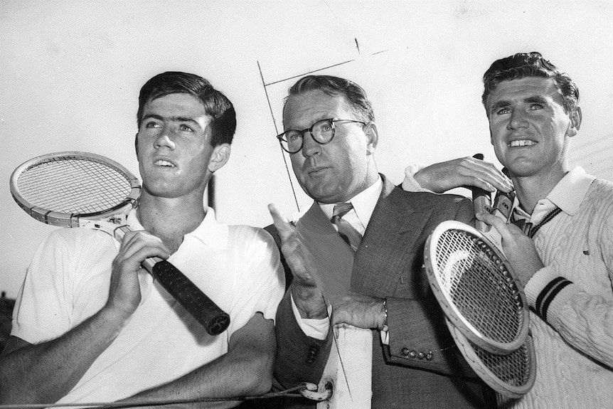 A black and white image shows three men staring into the distance pictured at a close range while holding tennis racquets.
