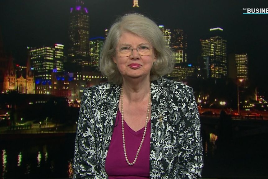 A woman wearing a black-and-white patterned jacket sits in front of a CBD backdrop in a TV studio.