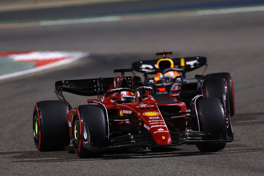 A red Ferrari race car leads a blue car on track in a race. 