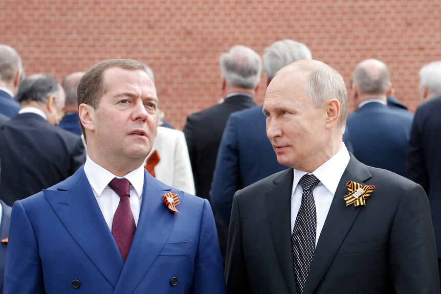 Medvedev and Putin stand side by side each with a ribbon pinned to their lapel. 