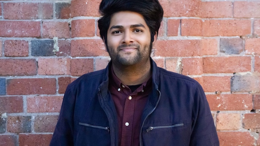 A man stands in front of a brick wall.