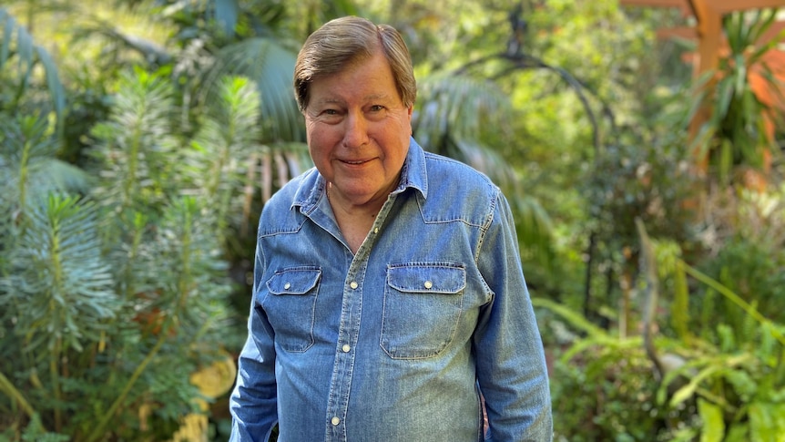 An elderly man standing in front of a garden