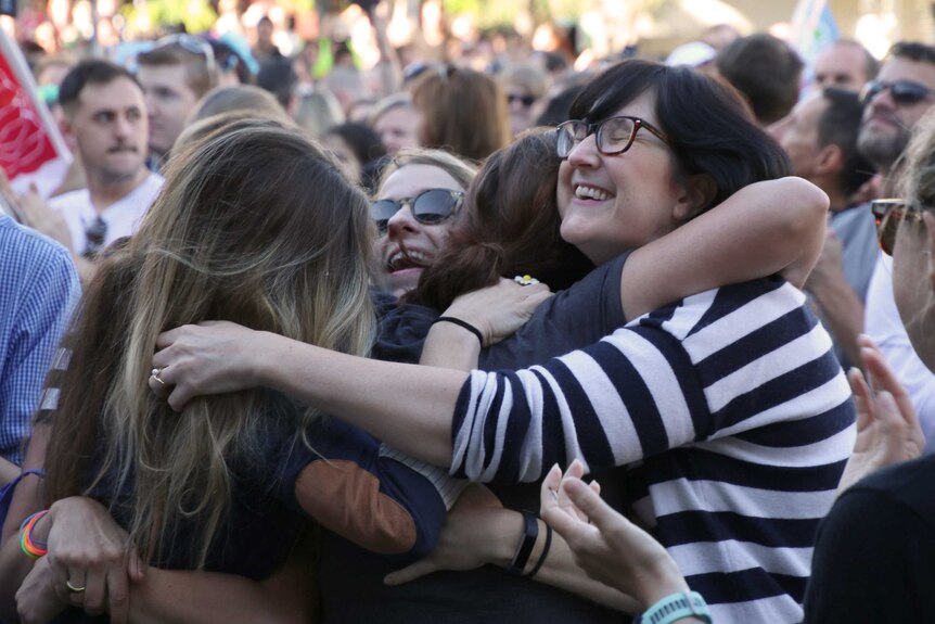 A group of women hug in a crowd with smiles on their faces after the results of the same-sex marriage survey were revealed.