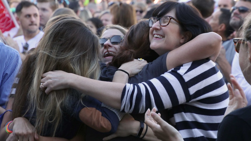 A group of women hug in a crowd with smiles on their faces after the results of the same-sex marriage survey were revealed.