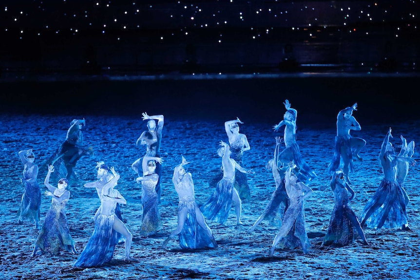 Dancers perform with blue patterns projected on them during the opening ceremony